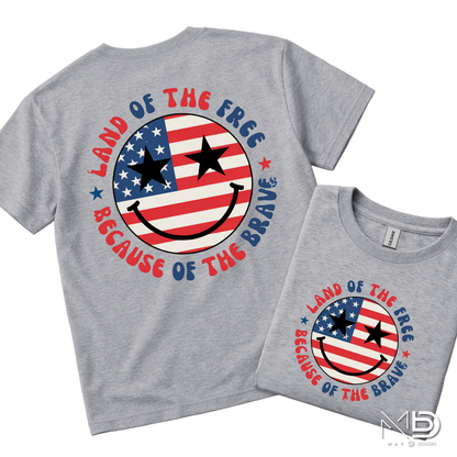 Land of the Free Because of the Braves Patriotic Smiley Face Shirt | American Flag Happy Face Tee | Fourth of July Graphic T-Shirt | USA Independence Day Shirt