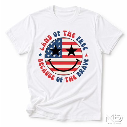 Land of the Free Because of the Braves Patriotic Smiley Face Shirt | American Flag Happy Face Tee | Fourth of July Graphic T-Shirt | USA Independence Day Shirt